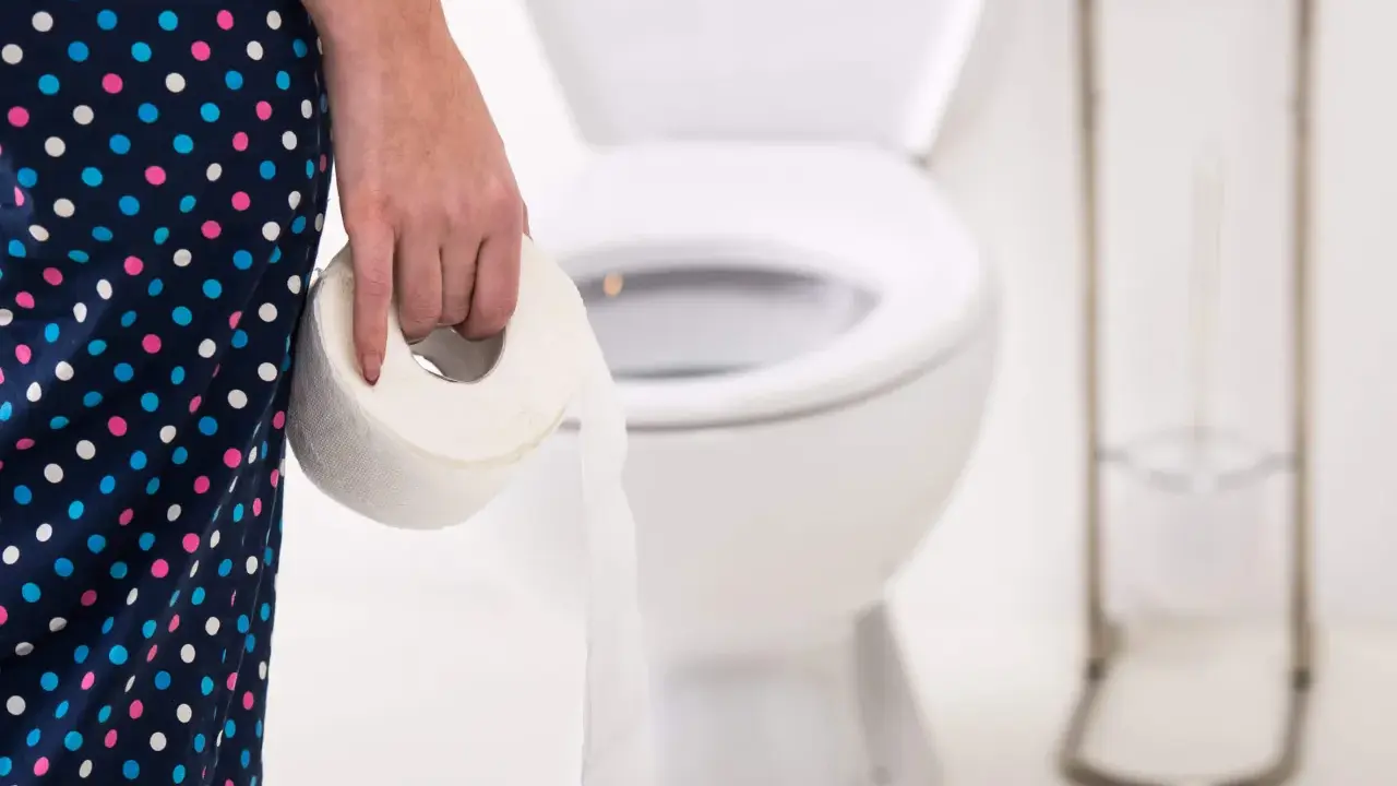 Osoba w kropkowanej piżamie trzyma rolkę papieru toaletowego, przygotowując się na nieuniknioną biegunka po alkoholu.