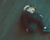 Młody mężczyzna skulony na drewnianej podłodze, wyrażający uczucie pustki i przygnębienia. Depresja po odstawieniu alkoholu odbija się na jego twarzy.