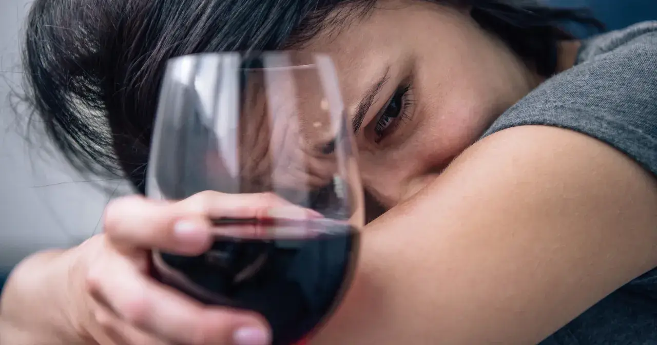 Smutna kobieta z kieliszkiem wina, odzwierciedlającym 6 objawów uzależnienia od alkoholu.