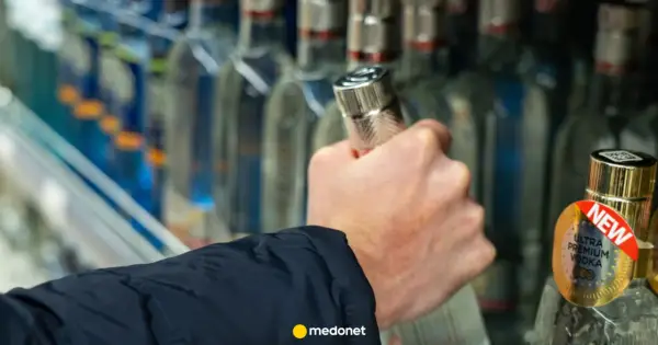 Dłoń sięga po butelkę wódki, a artykuł na medonet.pl analizuje wpływ alkoholu, w tym piwa, na białe krwinki.